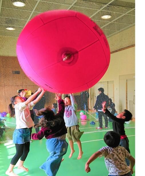 小平市ニュースポーツデーで、キンボールを楽しむ子供たちの写真。ピンク色の大きなボールを高く掲げています。