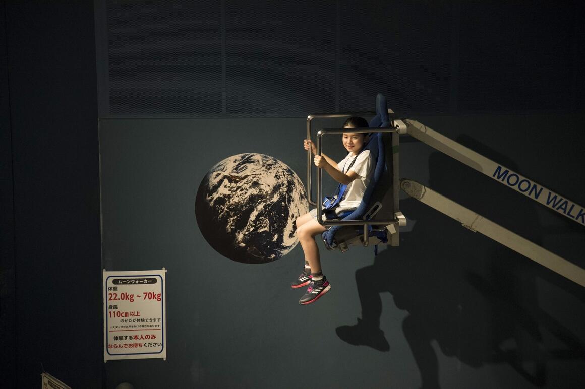 体験展示のムーンウォーカーに子供が乗って跳ねている写真。黒の背景に地球の写真が浮かび上がっています。